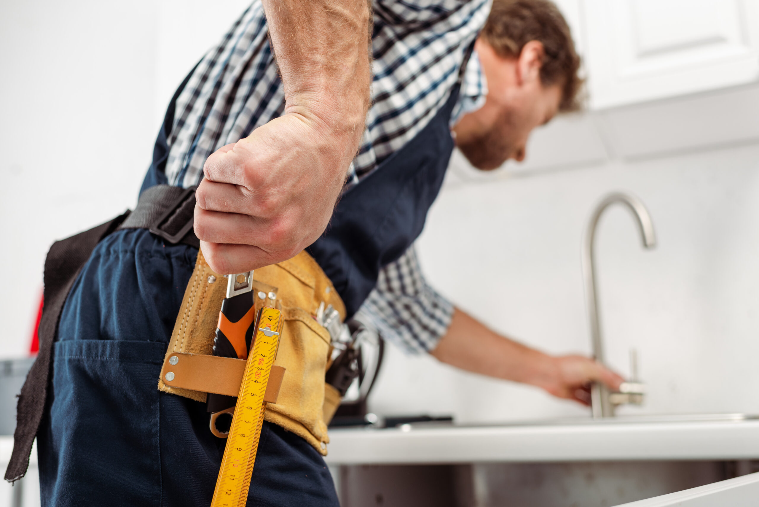 Selective focus of plumber taking wrench from tool belt while fi
